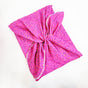 The pink Furoshiki from Waste Free Celebrations, featuring a colorful sprinkles pattern and light trim, is elegantly twisted and folded on a white background, providing a sustainable alternative to traditional gift wraps.