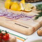 The Mizu Minimalist Chopping Board by WoodForChef, made from 100% FSC certified maple wood in Canada, engraved with the brand logo, holds sliced red onions and quartered lemons with cherry tomatoes and herbs nearby on a kitchen counter.