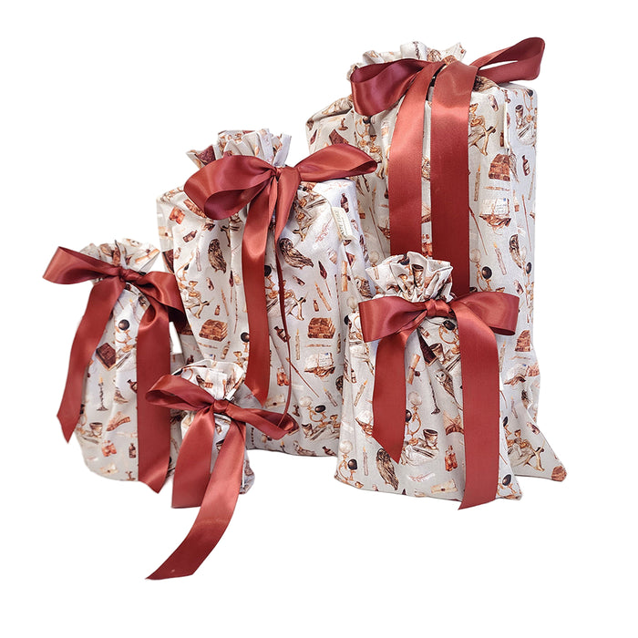Five Wizards and Wands reusable gift bags by Waste Free Celebrations, featuring vintage illustrations, are wrapped in white with red ribbons. The eco-friendly packages vary in size and are set against a plain white background, highlighting sustainable gift wrapping.