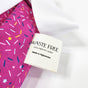 Close-up of a fabric label reading Waste Free Celebrations Made in Afghanistan, attached to a pink patterned fabric with multicolored sprinkles and a white section. Ideal for those who cherish the Reusable Gift Bags - Sprinkles sustainable wrapping option.