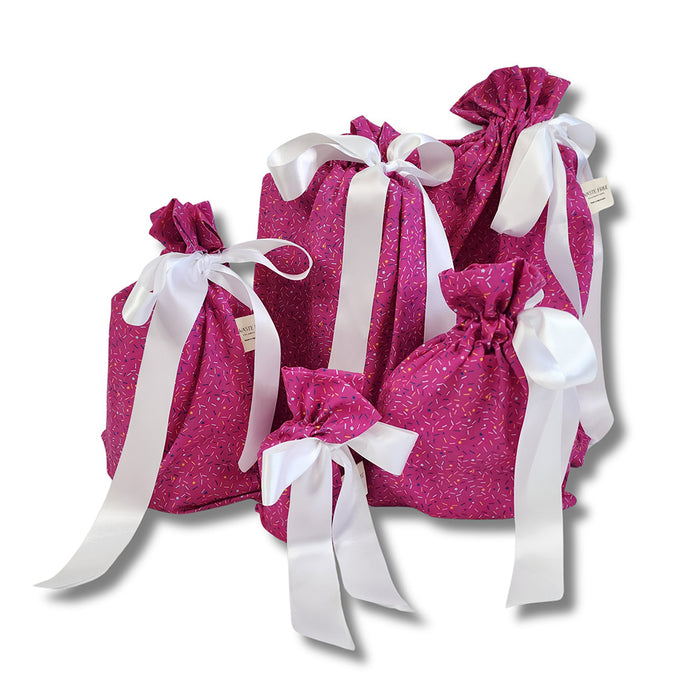 A set of six Reusable Gift Bags - Sprinkles by Waste Free Celebrations, in various sizes with white bows, features a subtle leaf pattern. Tied with ribbons on top, these eco-friendly bags are arranged together on a plain white background, offering a sustainable alternative to traditional wrapping.