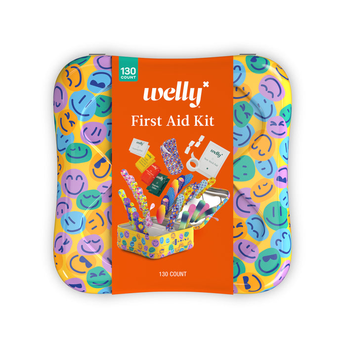 A cheerful Welly First Aid Kit tin with an orange label and smiling faces holds 130 assorted supplies, including organized ointments and flex fabric bandages, all arranged on a white background.