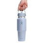 A hand grips the Flex Straw Cap of a 32 oz light blue Hydro Flask Wide Mouth Travel Bottle. With its insulated, sleek design and metal lid showcasing the central Hydro Flask logo, it stands out against a plain white backdrop, emphasizing its stylish and functional appeal as an essential accessory.