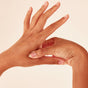 A person applies WTHN’s Body Balance Magnets to the skin between their thumb and index finger, stimulating acupressure points to enhance energy flow, against a light beige background.