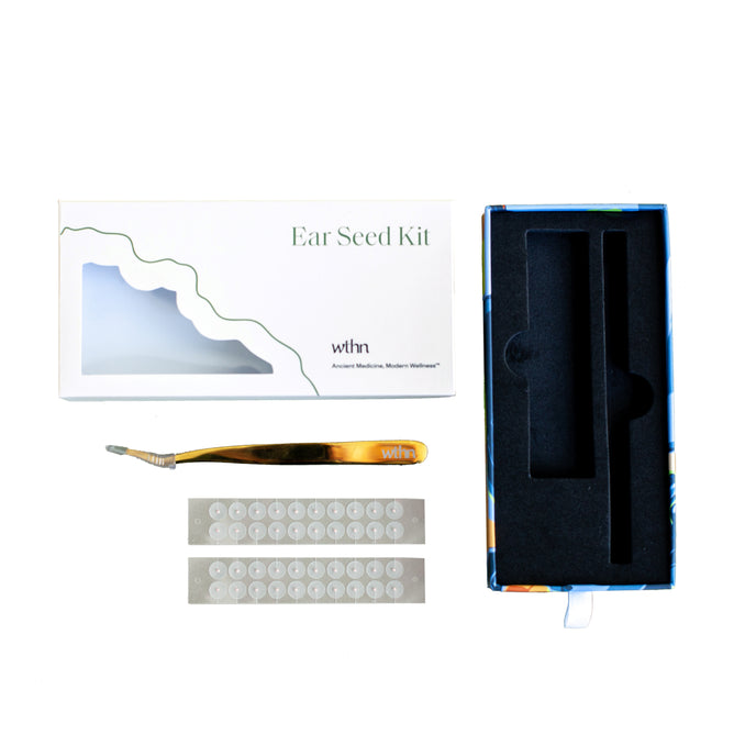 The WTHN Ear Seed Kit features a white box, gold tweezers, two adhesive ear seed strips, and an open foam-lined case. Inspired by Chinese medicine, these ear seeds are arranged on a white background for natural pain relief.