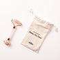A pink WTHN Face Roller Kit with rose gold accents, inspired by Traditional Chinese Medicine to reduce puffiness, rests beside a white pouch labeled FACE ROLLER KIT Ready, Set, Glow! on a white background.