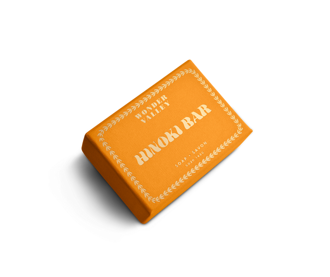 A rectangular orange Wonder Valley Hinoki Bar Soap, adorned with white leaf patterns and labeled “Hinoki Bar Soap/Savon,” rests on a white background.