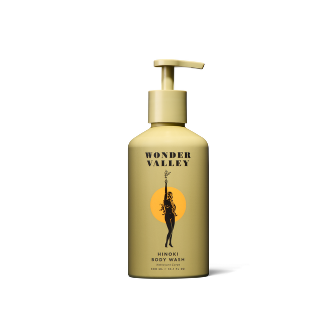 A yellow bottle of Wonder Valley Hinoki Body Wash with a pump, black text, and artwork of a person holding a branch before an orange circle, inspired by soothing hinoki and cedar wood scents.