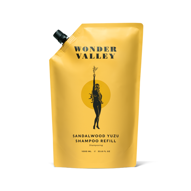 A yellow pouch labeled Wonder Valley Refill Hinoki Body Wash, featuring a black illustration of a woman holding a branch. The 1000 mL refill pairs perfectly with a refillable aluminum bottle and suits fans of hinoki fragrances.