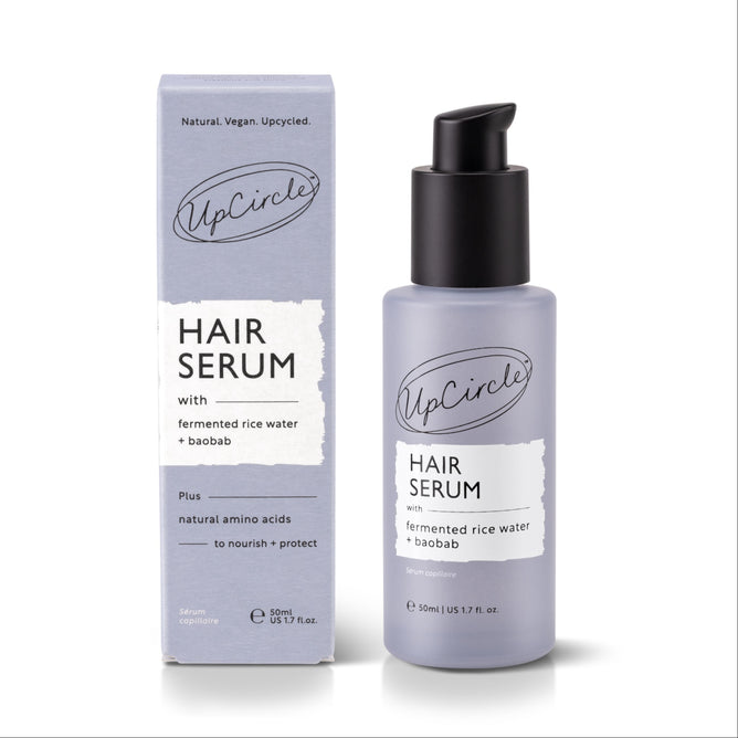 A bottle of UpCircle Hair Serum with Rice Water + Baobab stands beside its lavender box, which showcases product details and branding for frizz control.