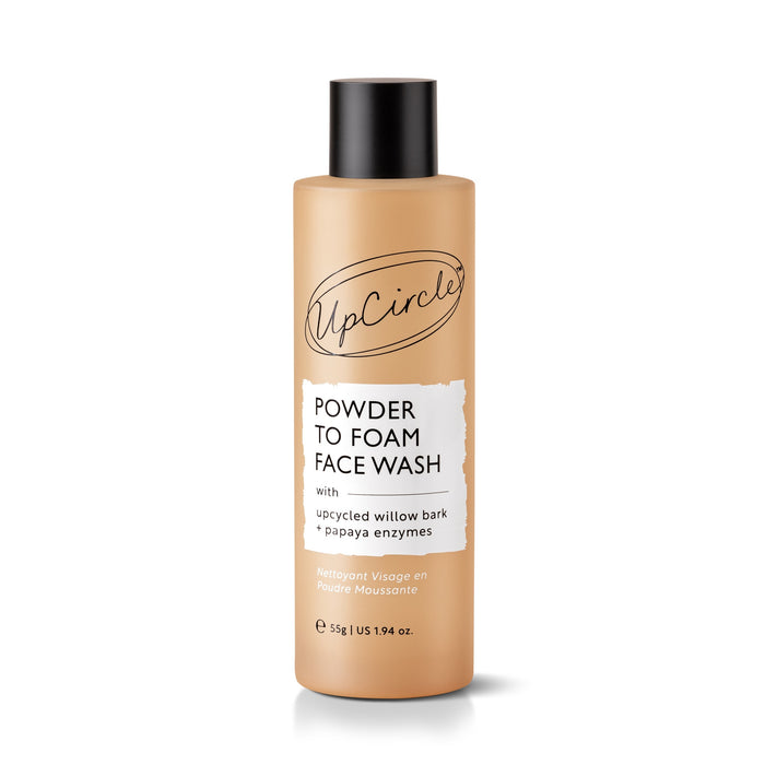 A tan bottle labeled UpCircle Powder To Foam Face Wash with Upcycled Willow Bark + Papaya Enzymes. The bottle has a black cap and contains 55g (1.94oz) of powder-to-foam cleanser, made with upcycled willow bark, rice lees, and papaya enzymes.