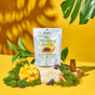 A bag of Plant People WonderBurn Gummies - For Metabolism & Cravings Control stands on a mossy rock, surrounded by cinnamon sticks, an amber bottle, mango, grapes, and tropical leaves with a yellow background.