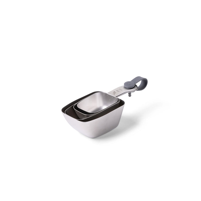 A set of three stainless steel, square-shaped measuring cups nested together, held by a metal ring with a gray silicone handle.