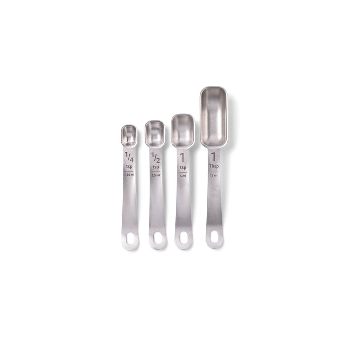 Four Full Circle stainless steel measuring spoons are lined up on a white background. This durable set features etched sizes: 1/4 tsp, 1/2 tsp, 1 tsp, and 1 Tbsp, along with milliliter measurements for precise cooking.