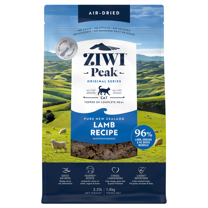 A bag of ZIWI Air-Dried Cat Food—All Natural, High Protein, Grain Free, Limited Ingredient with Superfoods—rests against New Zealand hills, its blue and white packaging highlighting it as a wholesome raw cat food alternative.