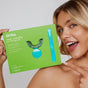 A smiling woman points to a green Zimba On-the-Go Kit box, which includes a mouthpiece, whitening gel tube, and LED accelerator light, set against a simple light background.