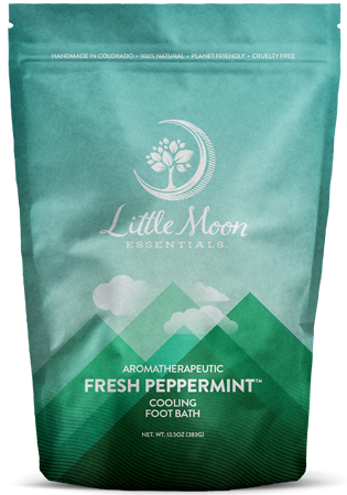 A teal and green resealable pouch labeled Little Moon Essentials Aromatherapeutic Fresh Peppermint Cooling Foot Bath with a mountain and sky design. The packaging highlights that it is natural, planet-friendly, and cruelty-free.