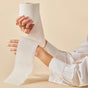 A person with multiple rings holds Caboos 2-Ply Bath Tissue against a beige background. Partially unrolled, the bamboo, tree-free toilet paper is presented by someone in a white shirt.