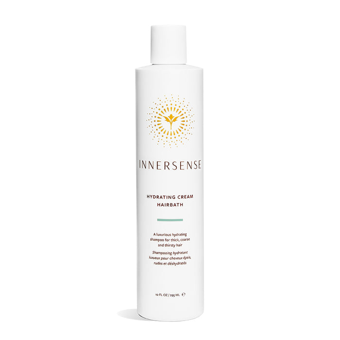 The Innersense Organic Beauty Hydrating Cream Hairbath comes in a white bottle with a golden flower logo above the text. This luxurious hydrating shampoo, made with organic ingredients, is ideal for thick, coarse, and thirsty hair. Capacity: 10 fl oz/295 ml.