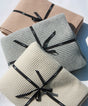 Three folded Adult Popcorn Blanket - Moonstone blankets in light gray, beige, and cream, each tied with a black ribbon.