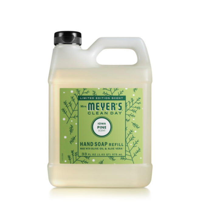 A clear plastic jug of Mrs. Meyer’s Clean Day hand soap refill in the Iowa Pine scent, featuring a green label with pine branch illustrations and a black cap.