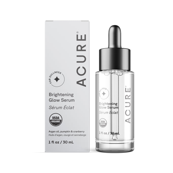 A clear glass bottle with a dropper labeled Brightening Glowing Serum by Acure is beside its white box. USDA organic-certified and containing 1 fl oz/30 mL, it provides antioxidant protection with argan oil, pumpkin, and cranberry.