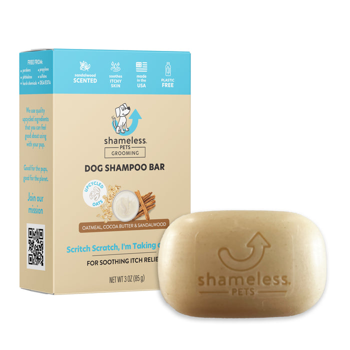 A Shameless Pets Dog Shampoo Bar with oatmeal, cocoa butter, and sandalwood sits in front of its packaging, which highlights that it is scented, made in the USA, and uses recycled plastic.