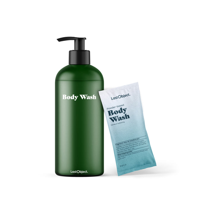 A green reusable bottle labeled Body Wash with a black pump, standing next to a blue and white sachet labeled Powder-based Body Wash by LastObject, on a white background.