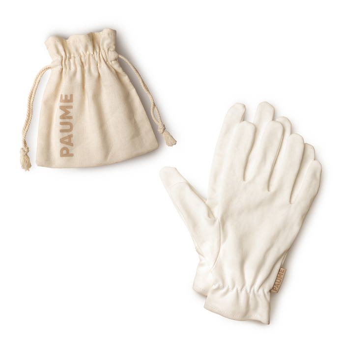 A pair of white gloves lies beside a small beige drawstring pouch with PAUME printed on it, both set against a white background.