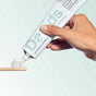 A hand squeezes Davids Hydroxi™ Premium toothpaste - Sensitive + Whitening w/nano hydroxyapatite from a tube onto a toothbrush with white bristles, set against a light background.