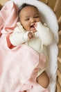 A baby in a cream-colored romper lies in a crib with a cream Little Love Blanket - Peony cashmere baby blanket.