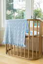 AU Baby Little Love Blanket - Hydrangea, a light blue organic cashmere baby blanket with a heart pattern and ruffled edge, draped over a wooden crib.