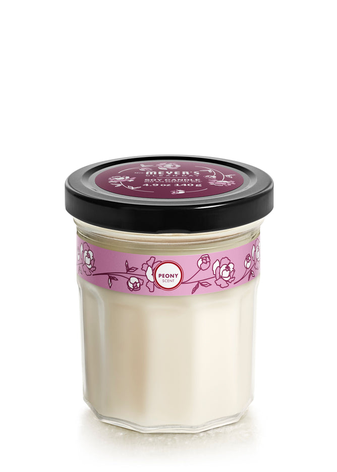 Mrs. Meyers Soy Glass Jar Candle boasts a creamy white vegetable soy wax in a hexagonal glass jar with a black lid. The clear jar has a pink floral label reading Peony. This product is cruelty-free.