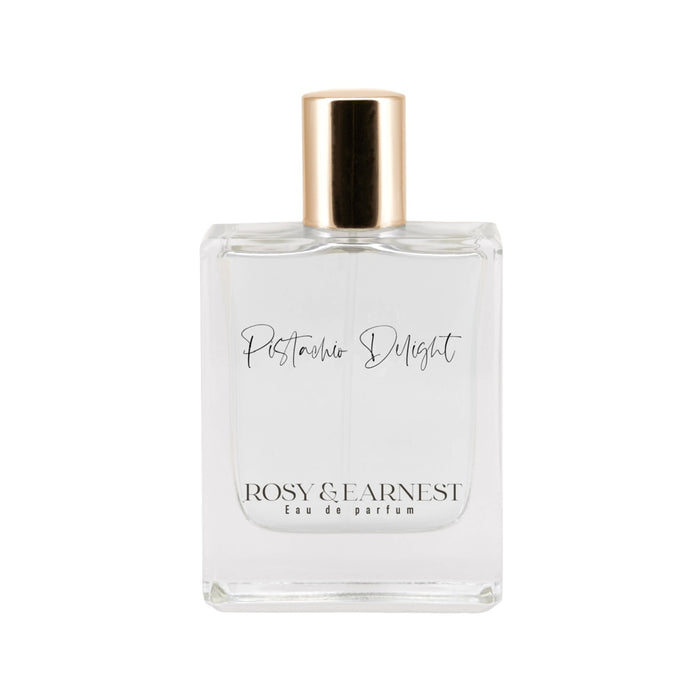 A clear glass perfume bottle with a gold cap. The label reads Pistachio Delight and ROSY & EARNEST Eau de parfum in black script and print fonts. The bottle is photographed against a white background.