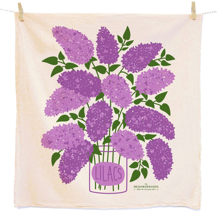 Illustration of a bouquet of purple lilacs with green leaves in a vase labeled “Lilacs” on a cream-colored cloth, hanging from a clothesline with wooden clothespins.