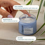 A hand scooping moisturizer from an open blue jar labeled Cliganic Barrier Boost Face Moisturizer, with on-screen text highlighting its hydrating and skin-plumping benefits—perfect as a daily face moisturizer. Soft-focus green plants are in the background.