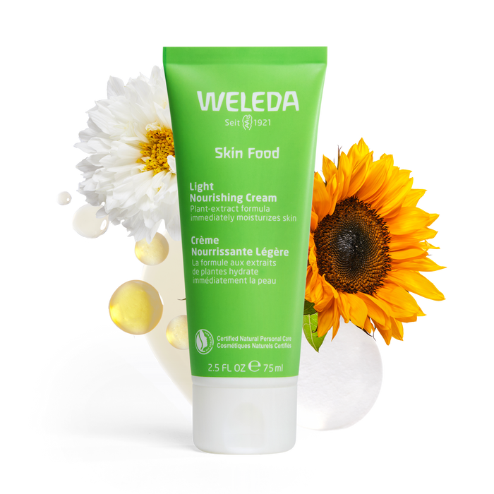 A green tube of Weleda Skin Food Light Nourishing Cream (75ml) is displayed upright with a white flower, a sunflower, and translucent cream droplets in the background. The packaging text is in English and French.