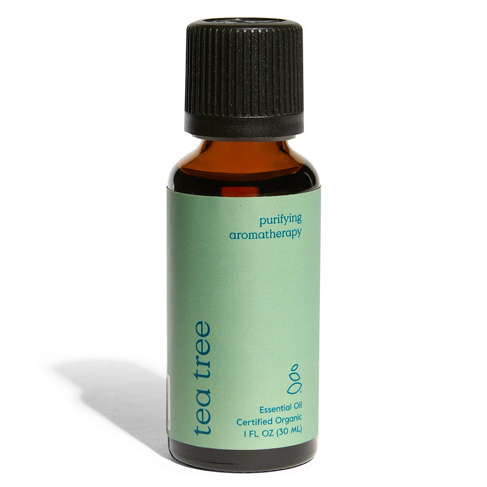 A small amber bottle with a black cap and a green label that reads tea tree, purifying aromatherapy, and Essential Oil Certified Organic 1 FL OZ (30 ML).
