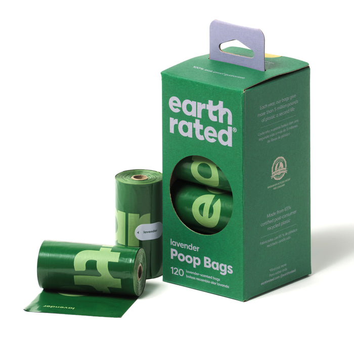 A green box labeled earth rated lavender Poop Bags with 120 bags, shown next to three green rolls of poop bags, one partially unrolled. The box features a handle and eco-friendly information.