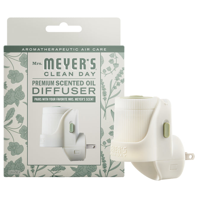 A Mrs. Meyer's Premium Scented Oil Diffuser is displayed before its packaging, which features botanical designs and product info. The white diffuser with a green accent fills your space with fresh, garden-inspired scents for a revitalizing atmosphere.