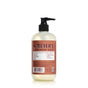 A bottle of Mrs. Meyers Clean Day hand soap with a pump dispenser, featuring a brown label with white and orange text and illustrations. The bottle is filled with a light-colored liquid and set against a white background.