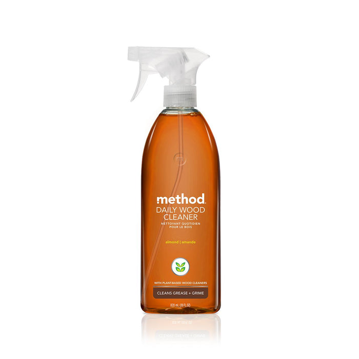 A clear spray bottle of Method Daily Wood Cleaner with an almond scent. The label is white with green accents and states it cleans grease and grime with a plant-based formula.
