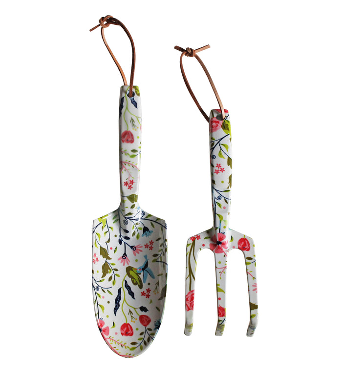 Two gardening tools with floral-patterned handles and leather hanging loops; a trowel on the left and a hand fork on the right, both decorated with colorful flowers and leaves.