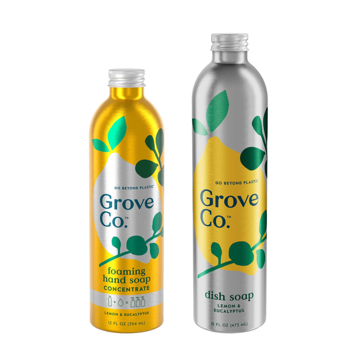 Two metallic bottles of Grove Co. Foaming Hand & Dish Soap Refills promise no plastic waste. The yellow bottle contains Foaming Hand Soap Concentrate, and the silver one has the Ultimate Dish Soap. Both feature green leaf designs and a refreshing lemon eucalyptus scent.