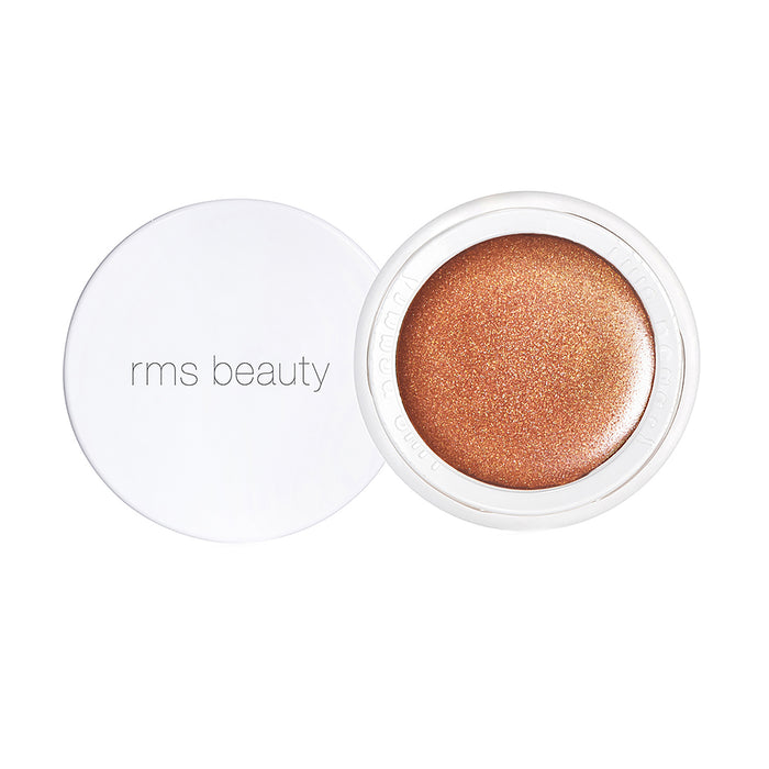 A round container of RMS Beauty makeup with a shimmery bronze product inside. The white lid, placed to the side, has rms beauty printed in gray lowercase letters.