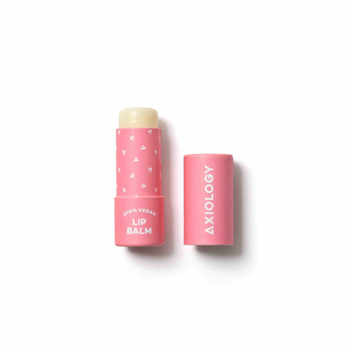 A pink tube of Axiology vegan lip balm with white text and small triangle patterns, shown with the cap off and placed beside the tube on a white background.