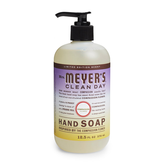 A 12.5 fl oz bottle of Mrs. Meyers Hand Soap offers a limited edition scent inspired by the compassion flower, with garden-inspired scents and essential oils, featuring purple text and a black pump dispenser.