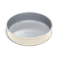 A round, light gray nonstick baking pan with high sides and a cream-colored exterior, featuring the brand name Caraway embossed on the inner bottom.