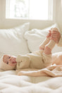 An adult holds the feet of a baby lying on an AU Baby Cashmere Cloud Baby Blanket Gift Set - Butter Cream, with the baby wearing a matching cream-colored bonnet, sweater, and socks.