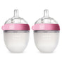 Two clear silicone baby bottles with pink rings and wide necks, each labeled comotomo, are shown side by side on a white background.